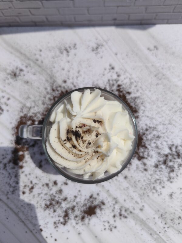 Vue de dessus de la bougie Cappuccino avec chantilly blanche au centre et chocolat en poudre saupoudré sur toute la surface.