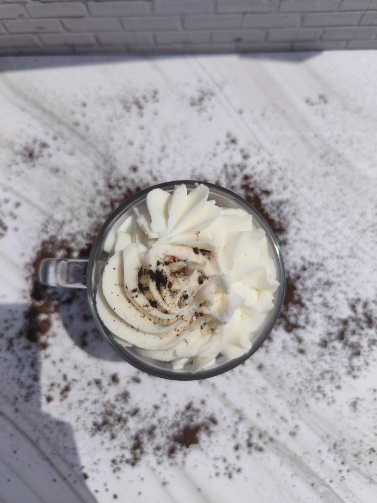 Vue de dessus de la bougie Cappuccino avec chantilly blanche au centre et chocolat en poudre saupoudré sur toute la surface.