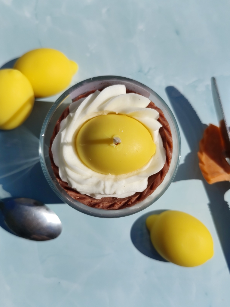Vue de dessus de la bougie Citron Meringuée avec gâteau en cire, coulis citron, citron entier au centre, chantilly blanche, décor avec couteau et citrons en cire autour.