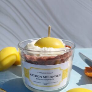 Bougie Citron Meringuée dans pot en verre avec gâteau en cire sur chantilly blanche, coulis jaune citron, crème pâtissière, citron entier au centre, citrons en cire et cuillère à côté.