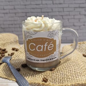 Bougie Café dans un pot en verre avec base marron, chantilly blanche et grains de café en cire. Cuillère à café posée à côté et grains de café dispersés autour.
