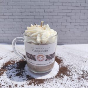 Bougie Cappuccino coulée dans une tasse en verre avec base marron, chantilly blanche au centre et chocolat en poudre saupoudré sur le dessus.