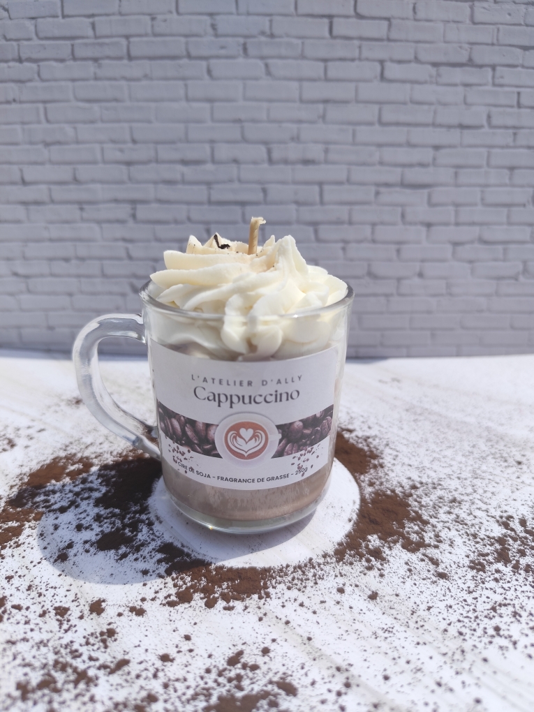 Bougie Cappuccino coulée dans une tasse en verre avec base marron, chantilly blanche au centre et chocolat en poudre saupoudré sur le dessus.