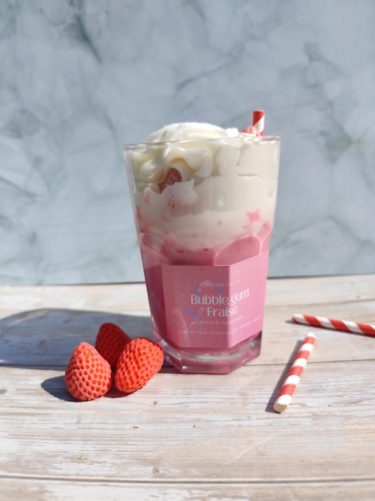 Bougie Bubblegum Fraise dans un pot en verre, base rose, chantilly blanche avec fraises en cire, paille rouge et blanche et paillettes argentées. Décor avec pailles et fraises en cire autour.