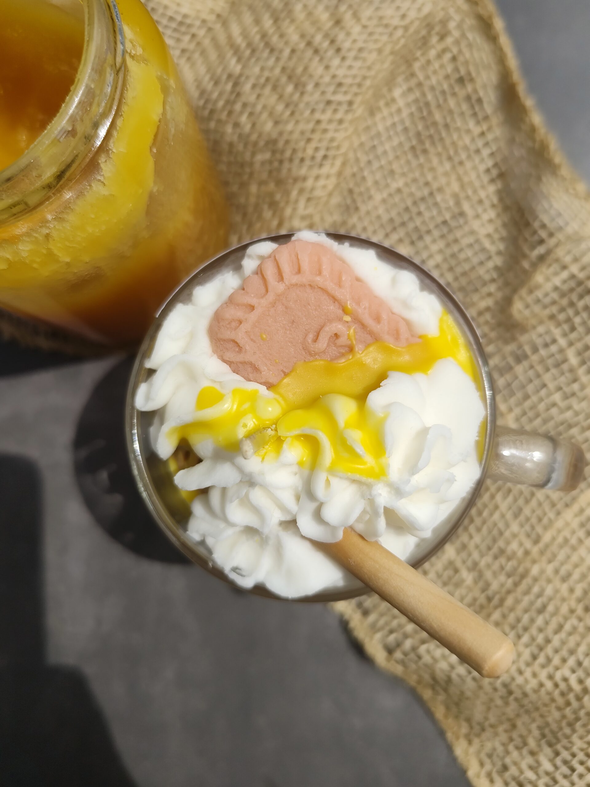 Vue de dessus de la bougie Café Blanc dans tasse en verre, avec chantilly blanche, coulis de miel, cuillère à miel et biscuit. Décor inspiré de la boisson libanaise.