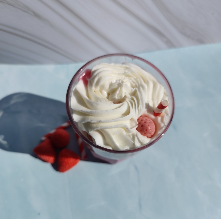 Vu de dessus de la bougie Bubblegum Fraise avec chantilly blanche, fraise en cire, paille rouge et blanche et paillettes argentées
