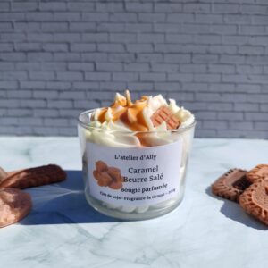 Bougie Caramel Beurre Salé dans pot en verre, avec chantilly blanche, coulis de caramel et tablette en cire couleur caramel. Décor gourmand avec biscuits autour.