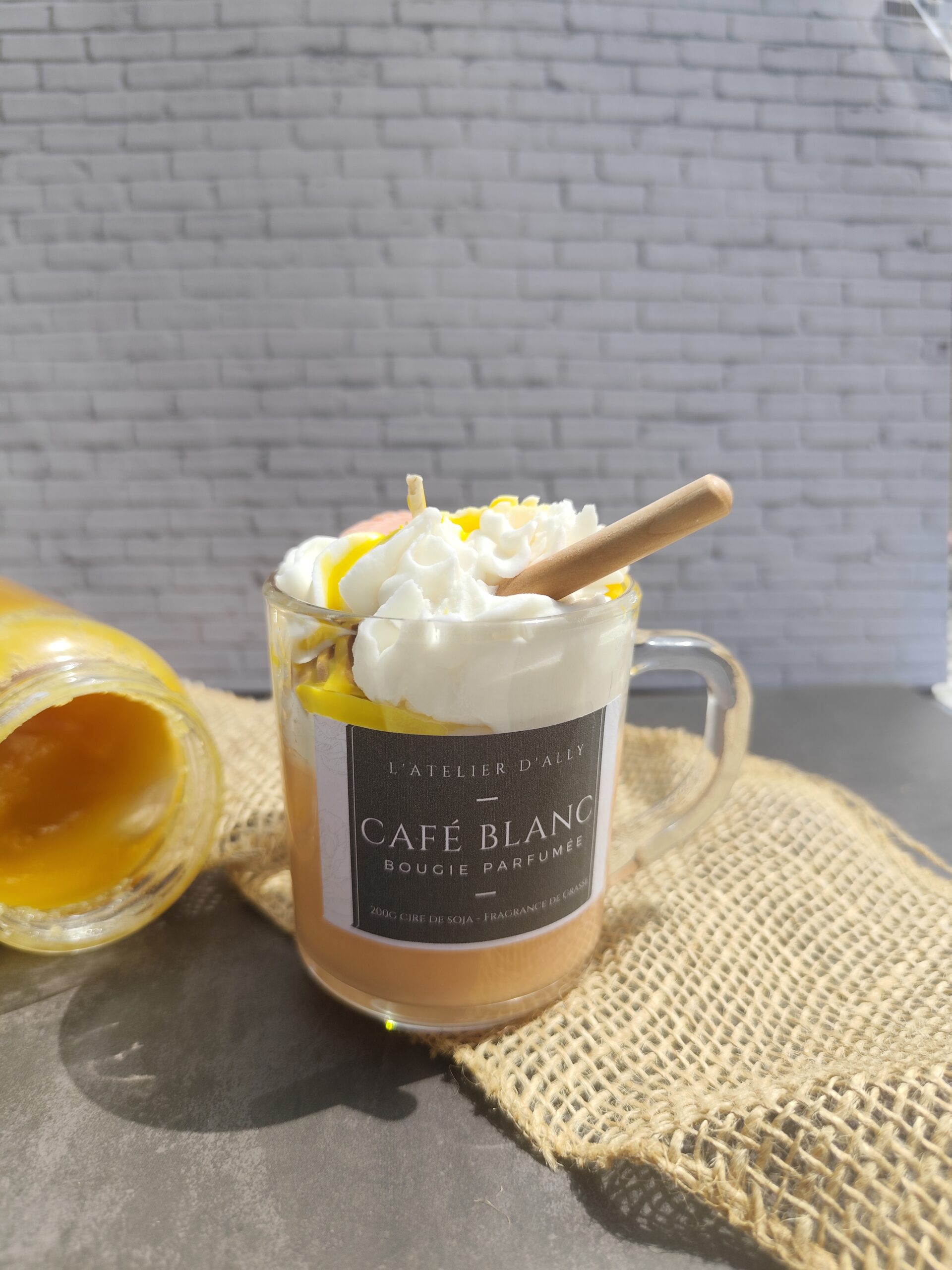 Bougie Café Blanc dans une tasse en verre, avec base orangée à la fleur d'oranger, chantilly blanche, coulis de miel, cuillère à miel et biscuit. Pot de miel en arrière- plan.