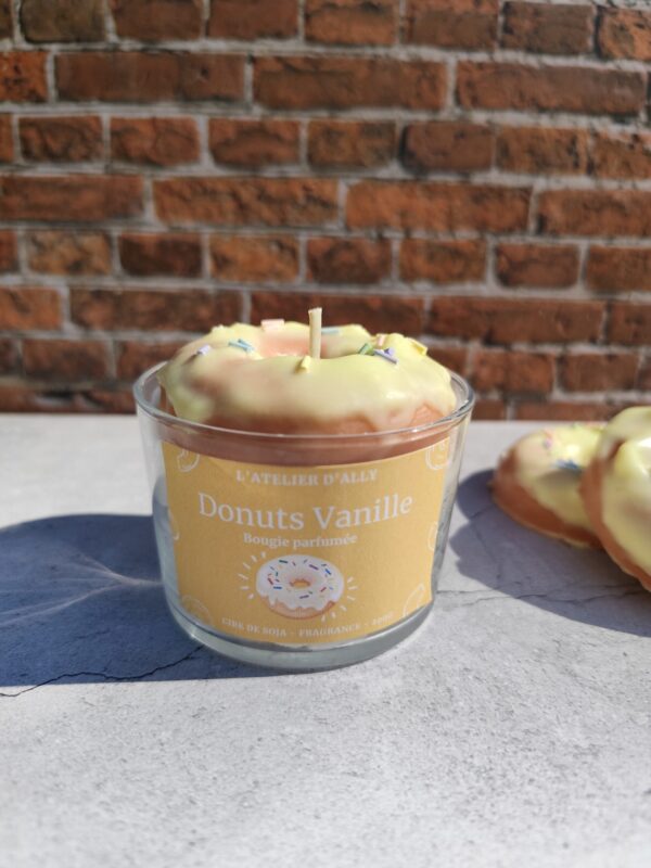 Bougie Donuts Vanille dans un pot en verre, décorée d'un donut en cire avec glaçage jaune et vermicelles colorés sur une chantilly blanche