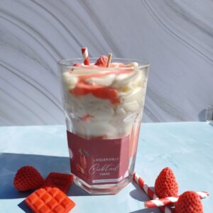 Bougie Cocktail Fraise dans son grand pot en verre, chantilly blanche, coulis rouge et fraise en cire avec paille rouge et blanche. Décor avec fraises en cire et tablette de chocolat rouge.