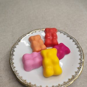 Cinq nounours fondants parfumés colorés présentés sur une assiette décorative.