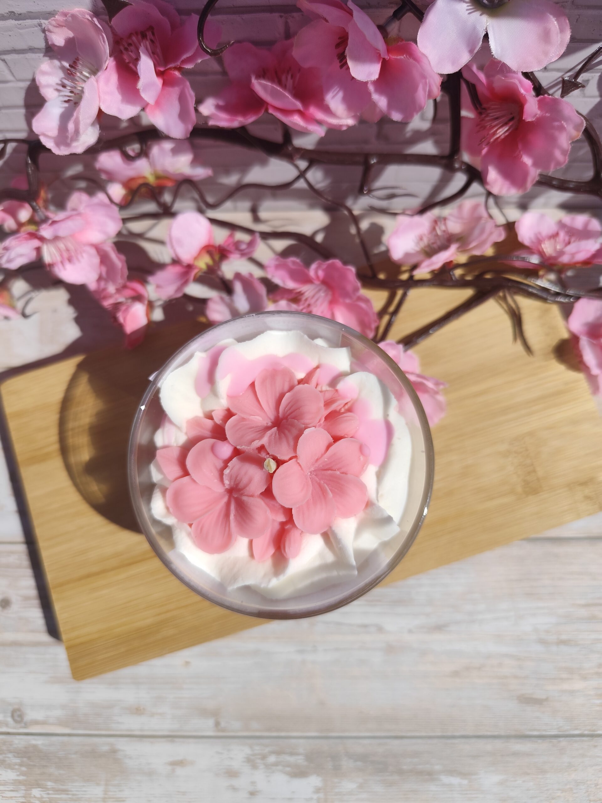 Vue de dessus de la bougie Fleurs de Sakura en cire rose façon sakura sur chantilly parfumée.