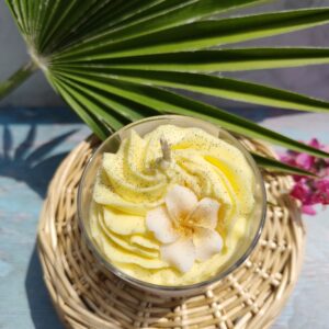 Dessus de la bougie Monoï Vanillé avec chantilly jaune, fleur d tiaré dorée et paillettes noires évoquant les grains de vanille.