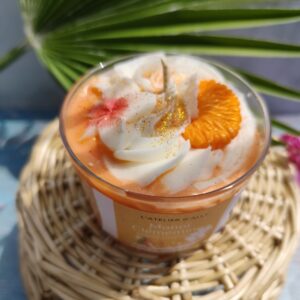 Bougie Monoï Clémentine sur panier en osier avec feuille de palmier, chantilly blanche et coulis orange décorée de clémentine en cire et fleur de tiaré.