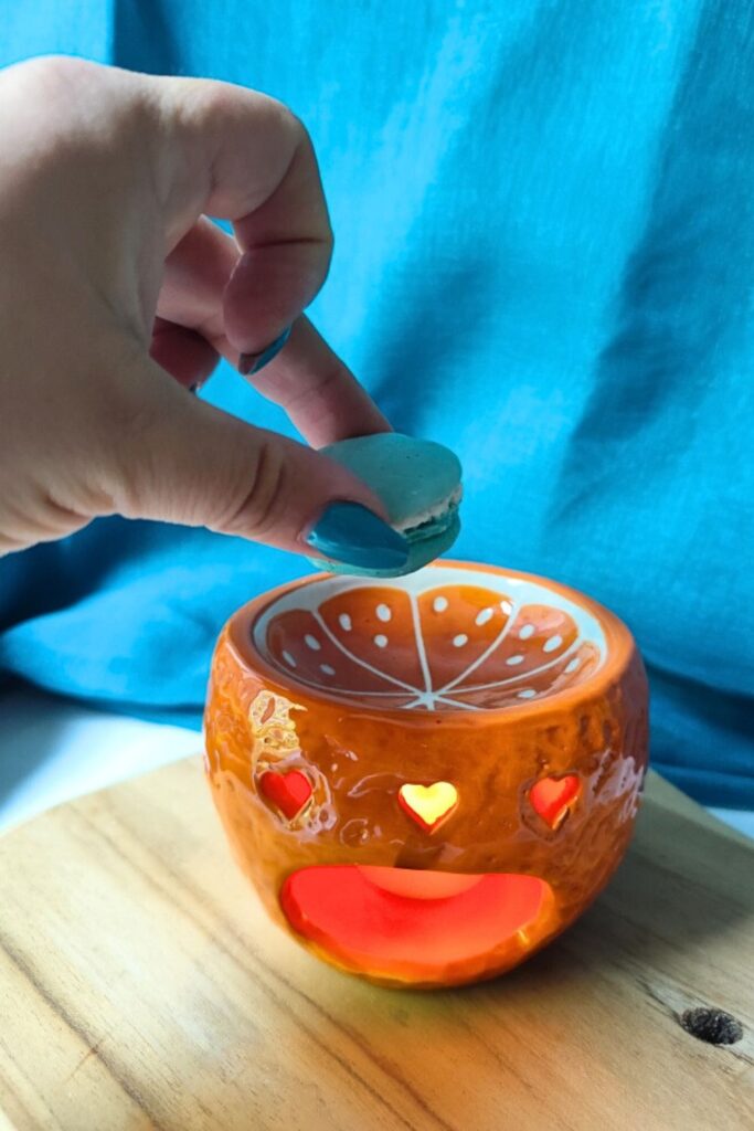 Main déposant un fondant parfumé en forme de macaron dans un brûleur orange allumé - L'atelier d'Ally