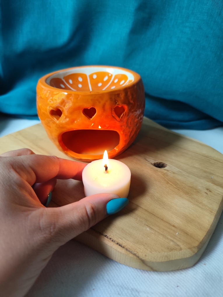Allumage d'une bougie chauffe-plat sous un brûleur orange en céramique pour fondants parfumés, précautions d'utilisation.