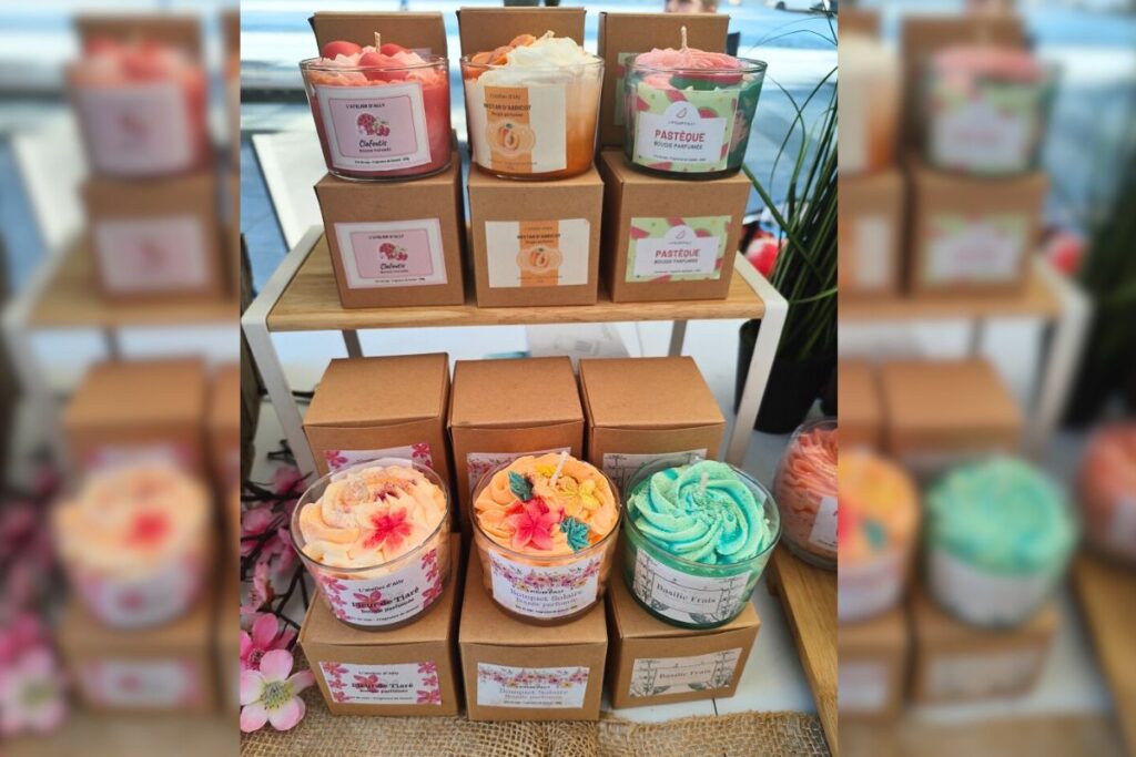 Bougies gourmandes parfumées exposées sur un marché, alignées sur des boîtes kraft avec fleurs décoratives -L'atelier d'Ally
