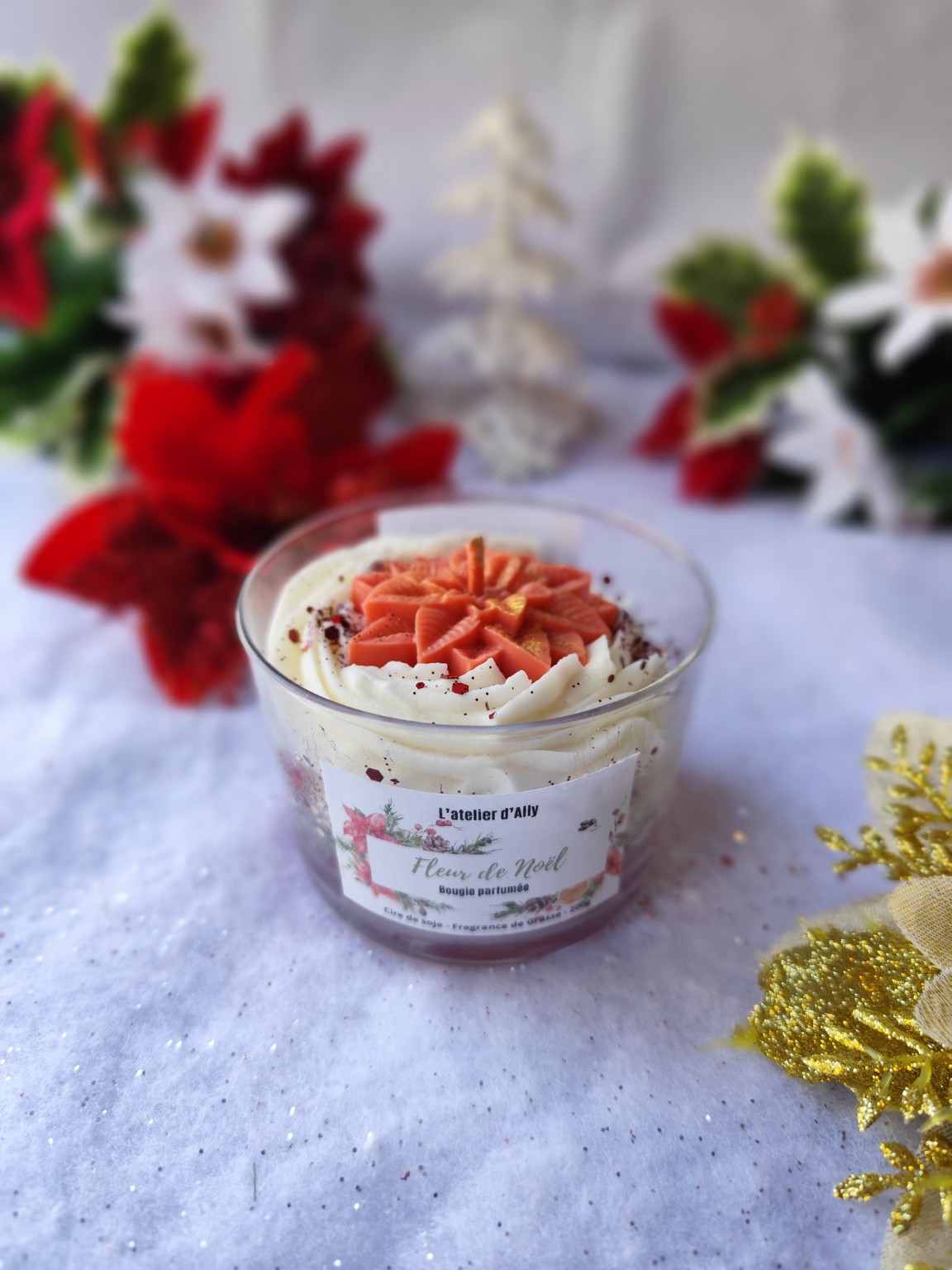 Gros plan sur la bougie Fleur de Noël et sa fleur de poinsettia rouge scintillante sur chantilly de cire.