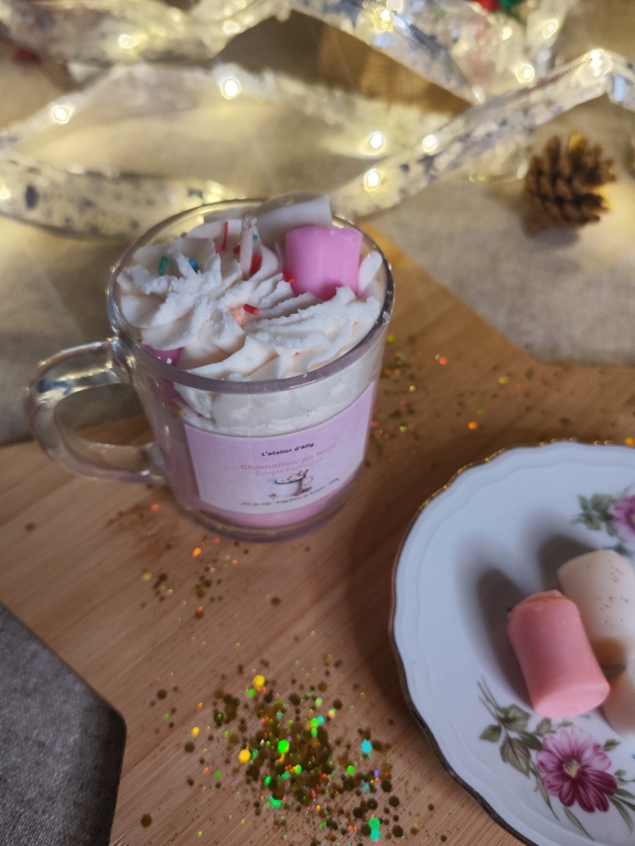 Bougie gourmande Chamallow de Noël posée sur une planche en bois avec paillettes et décorations lumineuses.