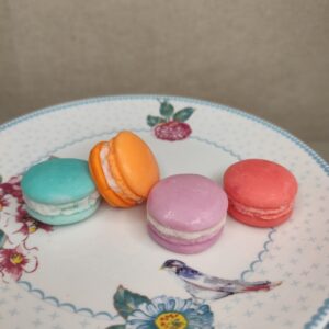 Assortiment de macarons fondants parfumés artisanaux aux couleurs pastel présenté sur une assiette fleurie.