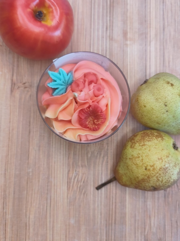 Vue aérienne de la bougie artisanale Grenade et Poire entourée d'une pomme rouge et de deux poires, mettant en valeur sa décoration colorée.