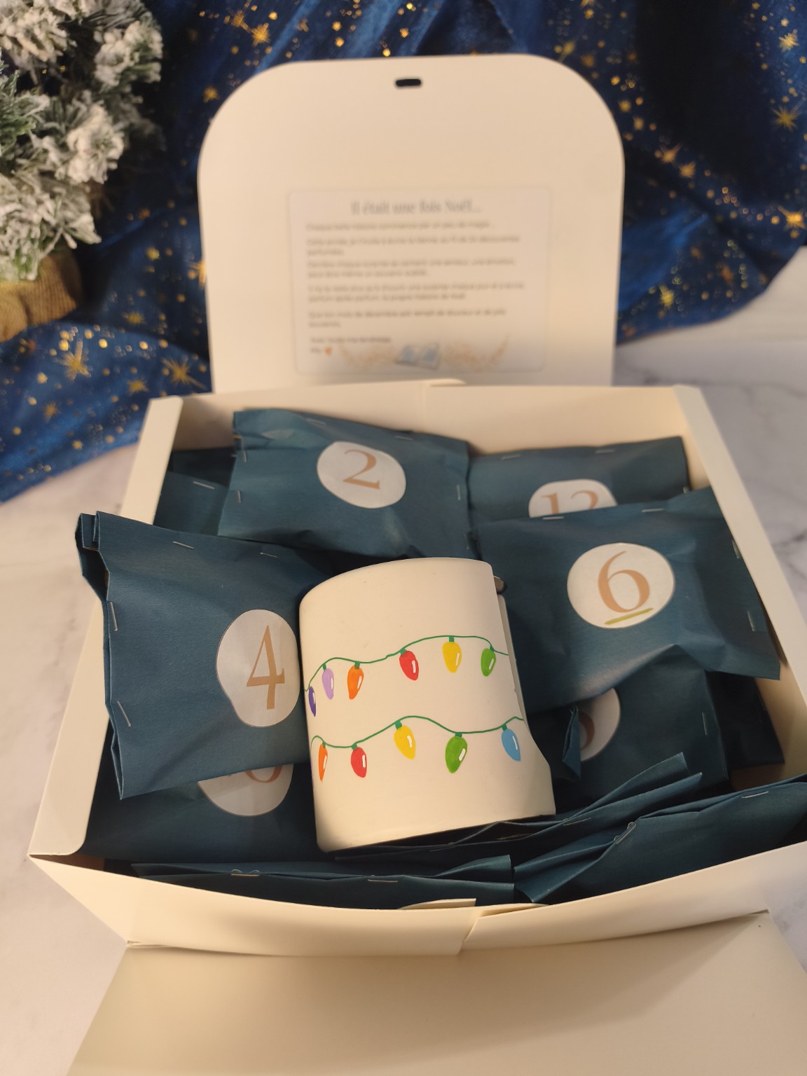 Brûleur artisanal de Noël décoré de guirlandes colorées, présenté dans le coffret avec les sachets numérotés du calendrier de l'Avent.