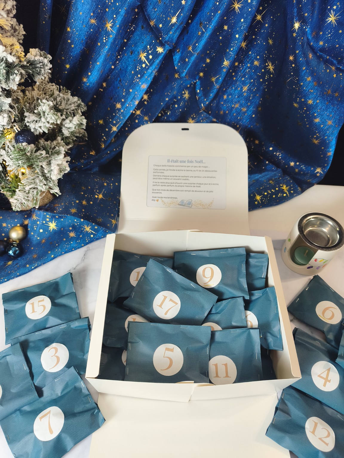 Calendrier de l'Avent ouvert avec ses petits sachets bleus numérotés, ses surprises parfumées et son brûleur de Noël.